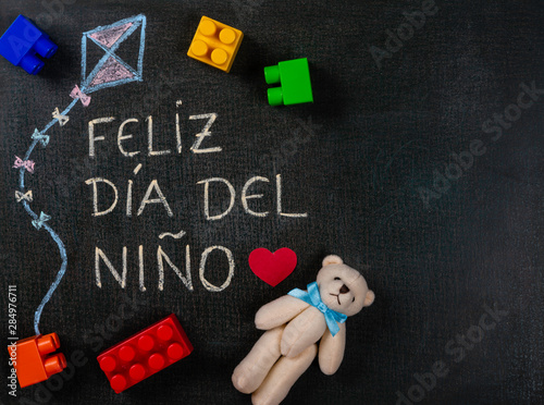 Blackboard written feliz dia del niño (spanish). Kite design with mounting parts and teddy bear. Copy space.