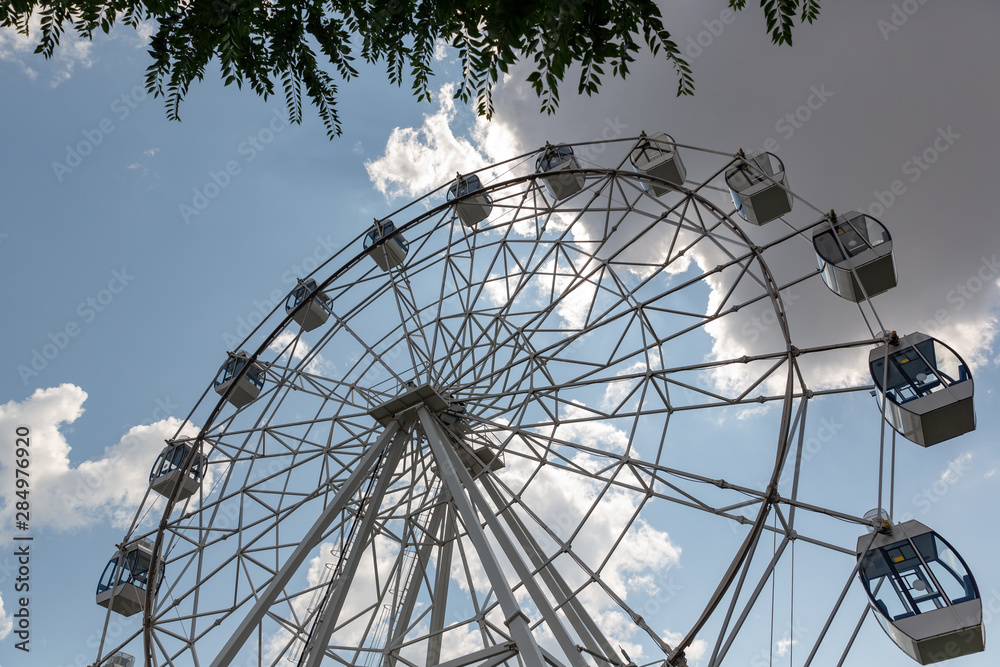 White Ferris wheel against a Sunny summer sky with white clouds.