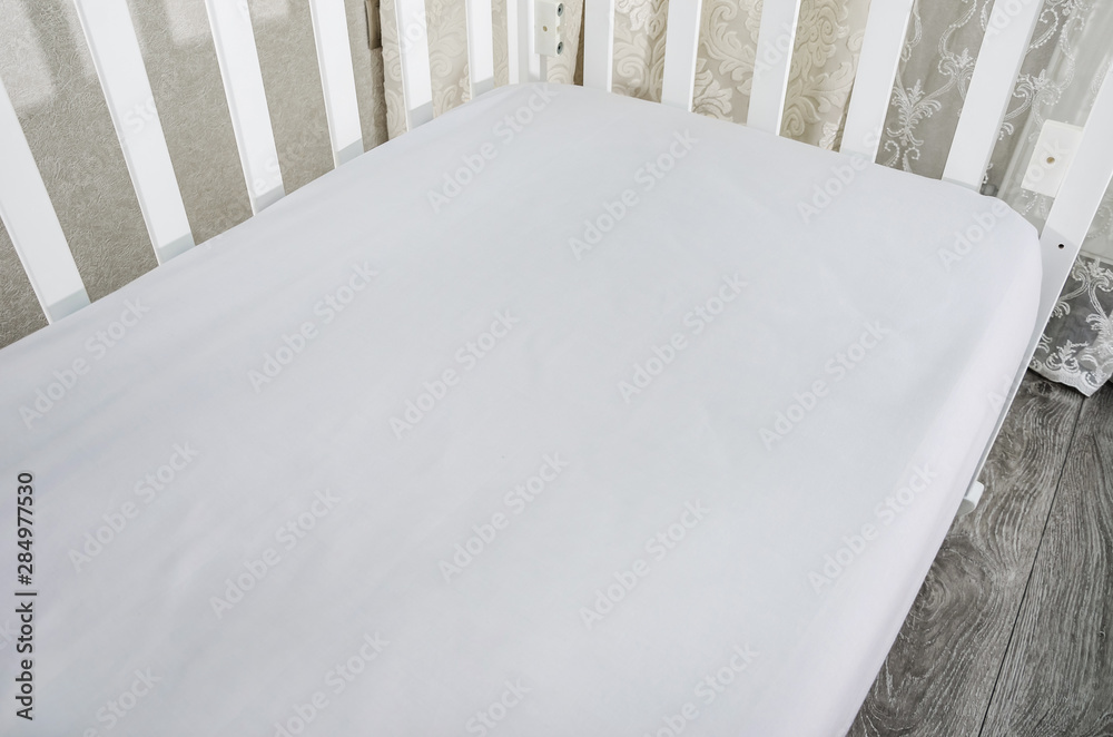 part of baby cot, close up. Mattress and sheets in white crib. part of baby cot, close up. Mattress and sheets in white crib.