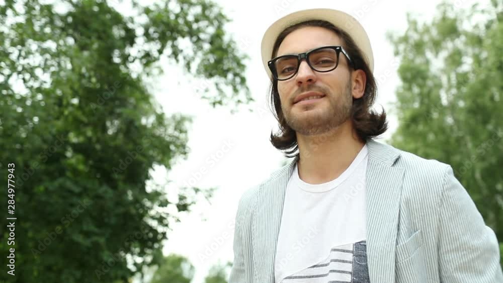 A handsome man in a hat walks through the Park wearing glasses and smiles. Men's fashion and beauty. Summer day. A handsome man in a hat walks through the Park wearing glasses and smiles. Men's fashion and beauty. Summer day.