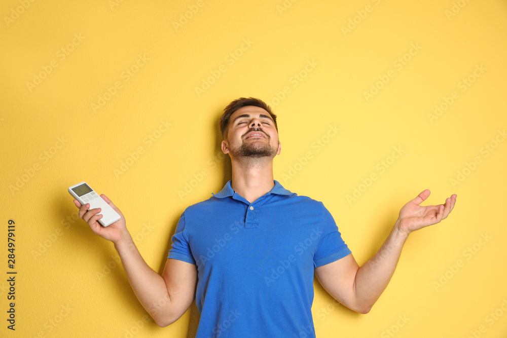 Happy young man with air conditioner remote control on yellow background Happy young man with air conditioner remote control on yellow background