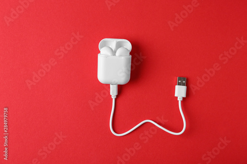 Modern wireless earphones in charging case with cable on red background, top view