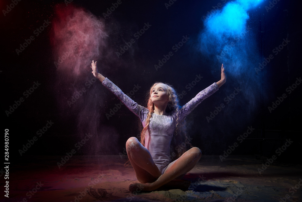 Beautiful teen girl with long blonde curly hair in a dark room with colored lights and clouds of flour