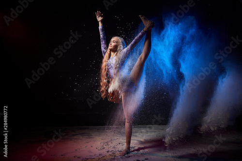 Beautiful teen girl with long blonde curly hair in a dark room with colored lights and clouds of flour