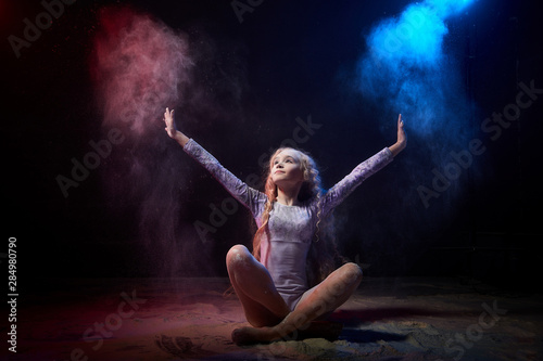 Beautiful teen girl with long blonde curly hair in a dark room with colored lights and clouds of flour © keleny