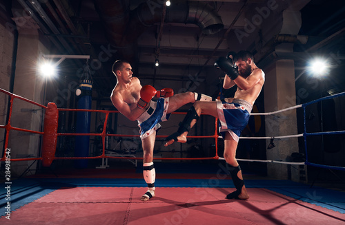 Two adult sportsmen kickboxers exercising kickboxing in the ring at the sport club