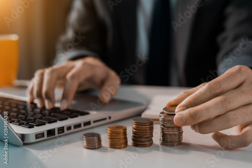 Businessman holding coins putting in glass with using laptop computer to calculate concept saving money for finance accounting in office. © NINENII