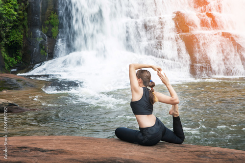 Young asain women practicing yoga at front of grand waterfall.