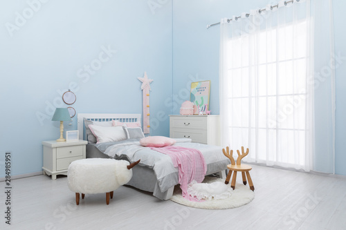 Children's bed in an empty room, lit by sunlight. There are white curtains, mats and jacquard quilts on the bed. photo