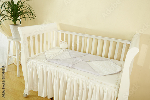 Children's bed in an empty room, lit by sunlight. There's a mat on the bed and a baby sleeping bag.