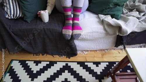 Legs of a girl on a sofa in warm multi-colored socks on a cold winter day in a Scandinavian interior. Hygge philosophy, the joy of home comfort