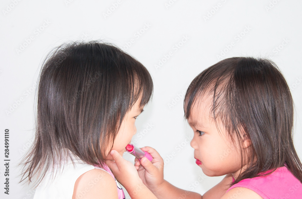 Asian child girl apply red lipstick on lips for sister on white background. Asian child girl apply red lipstick on lips for sister on white background.