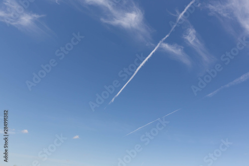 Two white jet tracks in a blue sky with sparse clouds. © Aleksandr