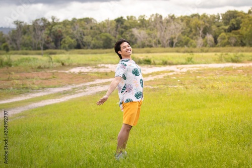 Happy asian man in Hawaiian shirt and yellow shorts stand on the sunny green field.