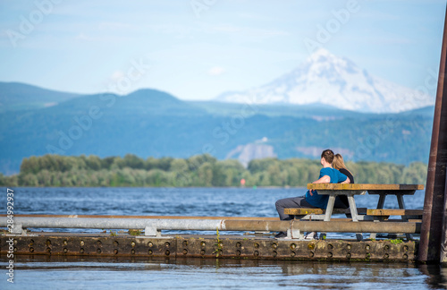 A guy and a girl are sitting on a bench on a floating dock on the Columbia River overlooking Mount Hood