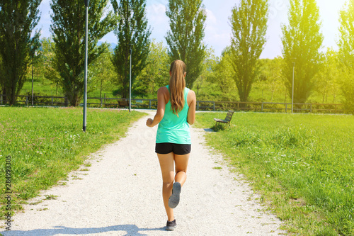 Young sporty woman running in park. Fitness girl jogging in park. Rear view of sporty girl running on pathway. © zigres