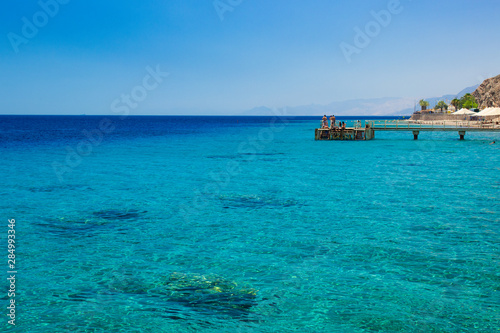 luxury resort coastline of Red sea Middle East scenery landscape view with wooden pier and resting people, coral riffs on bottom 