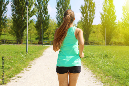 Young sporty woman running in park. Fitness girl jogging in park. Rear view of sporty girl running on pathway.