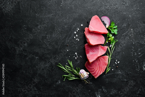 Raw tuna fillet. Seafood on a black stone background. Top view. Free copy space.