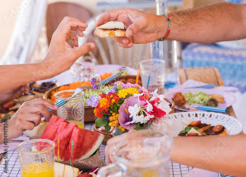Sharing food with the family. Caucasian peoples enjoying brunch or meal together. Fruits and vegetables on the wooden table. Sunlight outdoor on the terrace