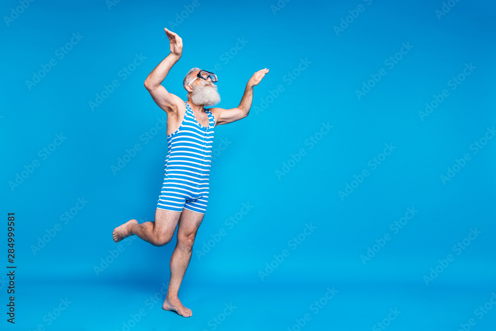 Full length profile side photo of concentrated pensioner swimming up with underwater equipment wearing swim wear isolated over blue background Full length profile side photo of concentrated pensioner swimming up with underwater equipment wearing swim wear isolated over blue background