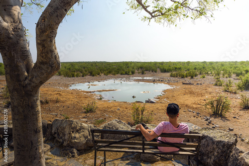 Foto Tourist waits for wildlife at the Moringa waterhole near Halali, Etosha, Namibia