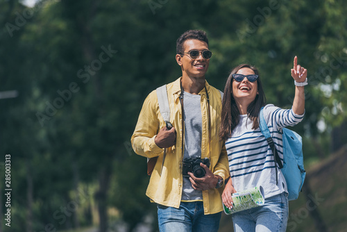 happy girl in sunglasses pointing with finger near mixed race man with digital camera © LIGHTFIELD STUDIOS