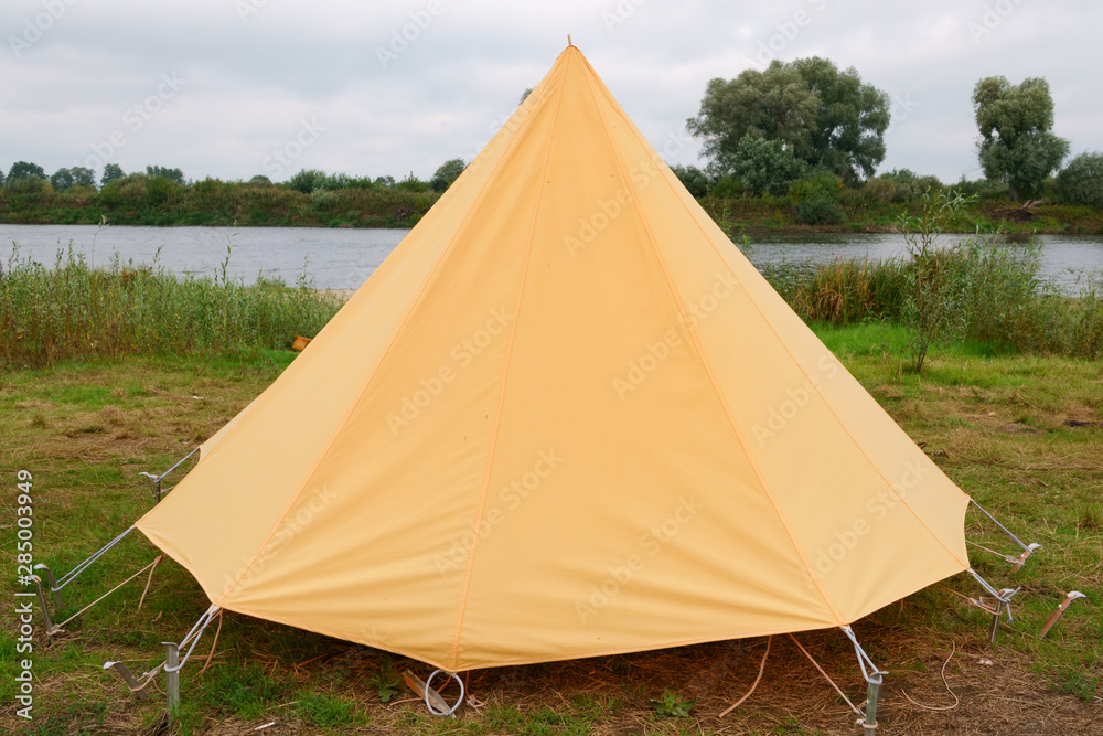 Old yellow canvas camping tent with iron pegs.