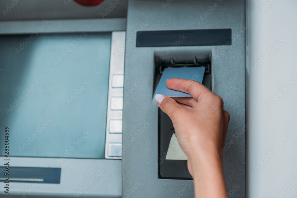 cropped view of woman putting credit card into atm machine cropped view of woman putting credit card into atm machine