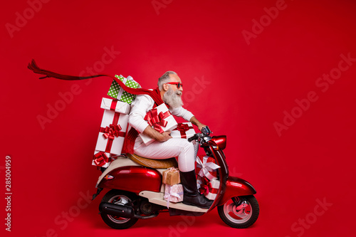 Profile side view of his he nice attractive stylish cheerful cheery gray-haired man riding driving bike delivering shop sale discount boxes isolated over bright vivid shine red background