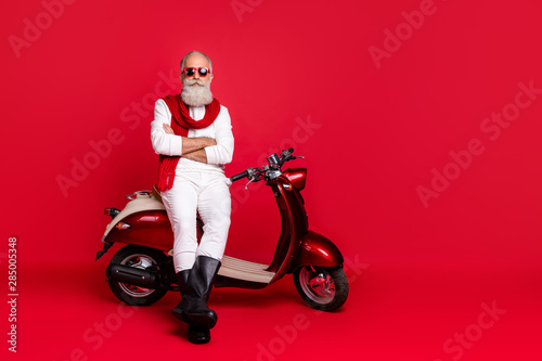 Amazing aged man sitting on retro moped with crossed arms wear jumper and trousers isolated red background