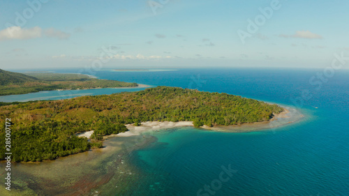Seascape: shore of island Balabac with forest and palm trees, coral reef with turquoise water, top view. Coastline of tropical island covered with green forest against the blue sky with clouds and
