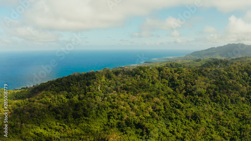 Coastline of tropical island Balabac covered with green rain forest against the blue sky with clouds and blue sea, aerial view. Seascape: Ocean and sky. Palawan, Philippines