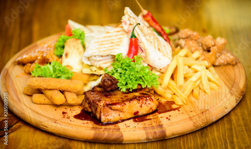 Wooden board french fries fish sticks burrito and meat steak served with salad. Pub menu snack. Enjoy your meal. Meat snack for group friends. Tasty delicious snacks. Restaurant food. Snack for beer