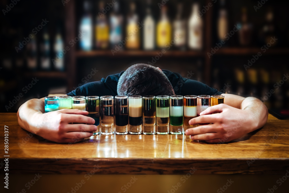 Drunk man fell asleep at the bar near different short drinks with