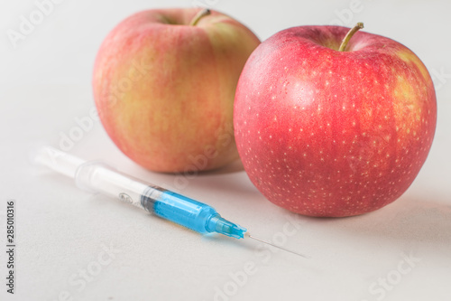 GMO and junk food concept. Apples and medical syringe with a chemical preparation on a white background