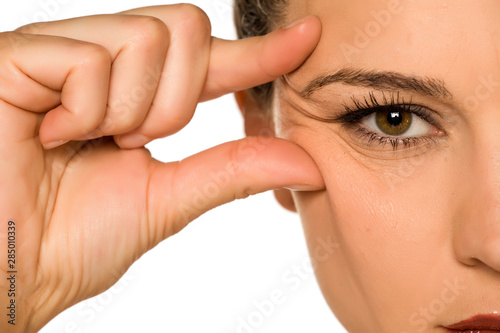 young woman pinching her eye wrinkles with her fingers on a white background photo