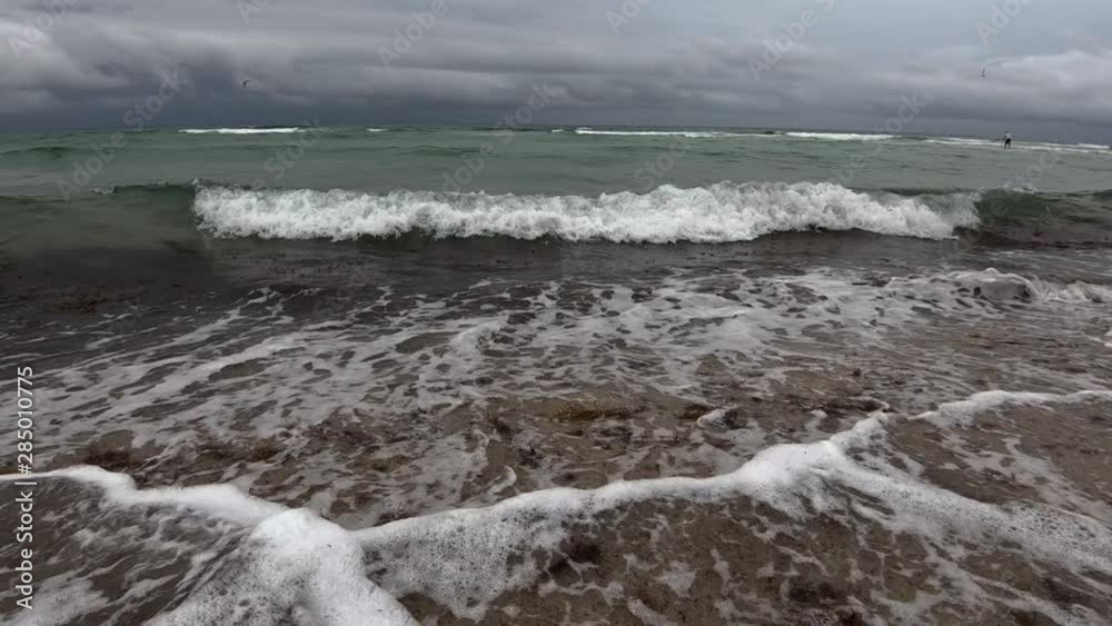 Slow motion low angle tidal waves hitting fine sand shore on rainy day, person on SUP, Miami Beach, Florida