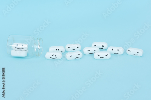 Pills with funny faces and a glass bottle on a blue background. Pharmacy antibiotic. Treating with antidepressant. Mental disorder. The concept of antidepressants and healing. Copy space.