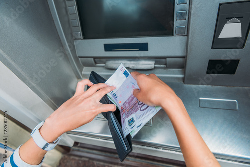 top view of woman putting money in wallet near atm machine