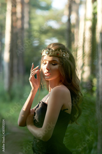 young, beautiful girl in a black dress with a crown in the forest © Mihail