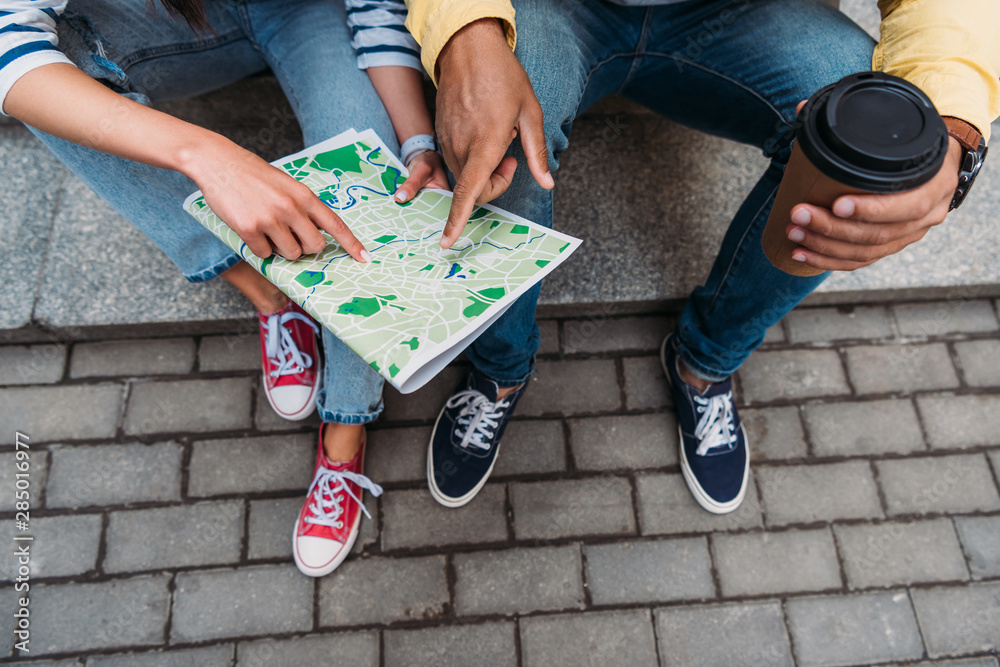 Obraz premium Cropped view of bi-racial man pointing with finger at map near woman sitting on stairs