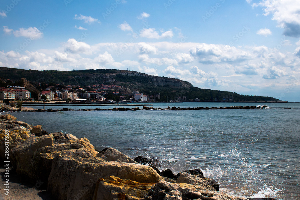 Seascape - light waves, stones on the embankment, they say, a seaside town on a mountain background Seascape - light waves, stones on the embankment, they say, a seaside town on a mountain background