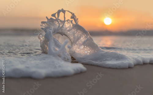 Glaskugel am Strand in der Schaumwelle im Sonnenuntergang