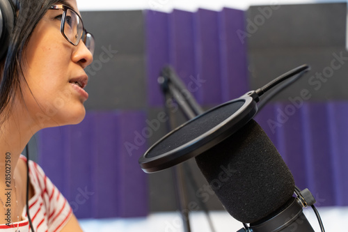 Asian woman with eyewear speaking in front a microphone.
