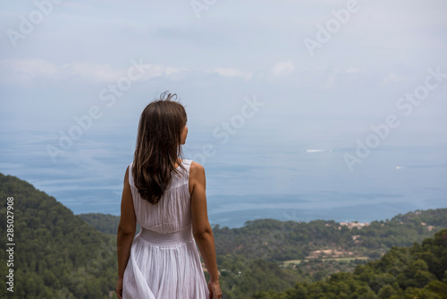 Cap de Formentor, Mallorca, Spain. Young woman in front of beautiful scenery with the sea, rocks and cloudy sky.