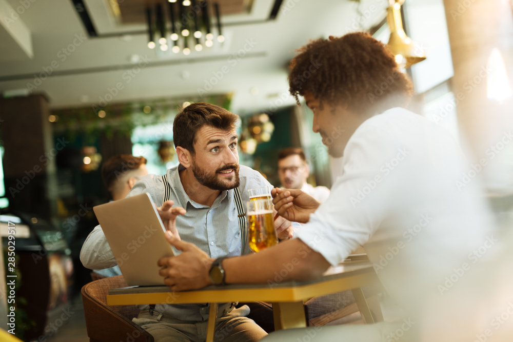 Men are sitting at table in modern cafe. Talk about work