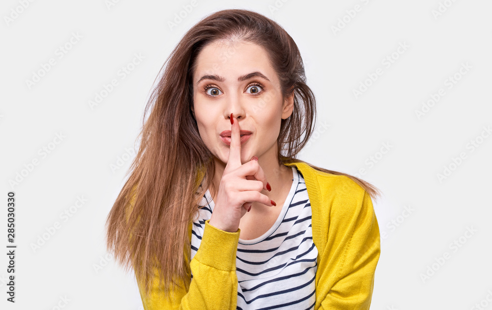 Closeup studio portrait of pretty young woman wears casual outfit, holding index finger on lips, asking to keep silence. Caucasian student female asks to be quiet. Closeup studio portrait of pretty young woman wears casual outfit, holding index finger on lips, asking to keep silence. Caucasian student female asks to be quiet.