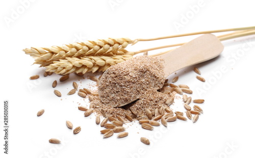 Spelt bran and grains with wheat ears and wooden spoon isolated on white background photo