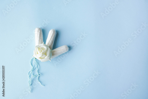 tampon menstrual cotton pads on blue background copy space with white flower . Woman hygiene conception photo, gynecological menstruation cycle .